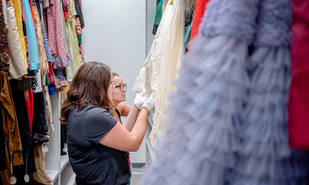 Students inspect a piece of clothing hanging on a rack of historic costumes